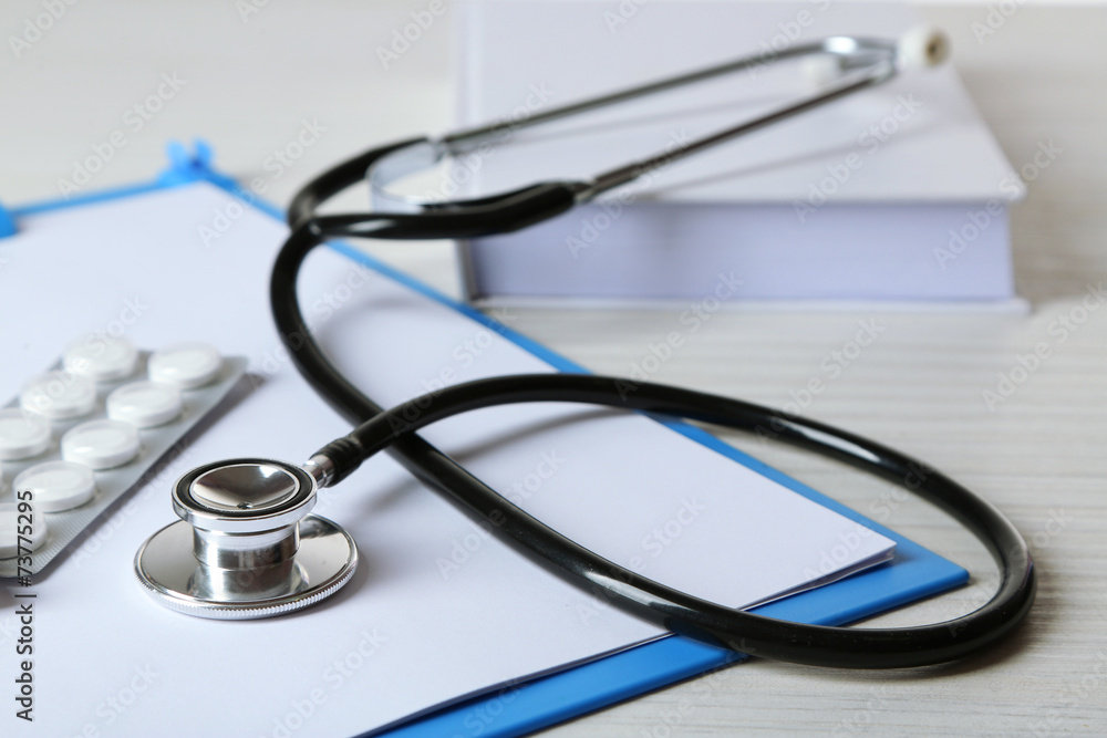Medical stethoscope with book and folder on wooden table Medical stethoscope with book and folder on wooden table