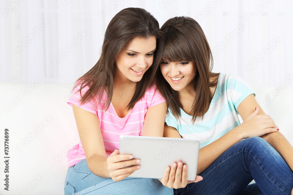 Beautiful girls twins with electronic tablet on sofa Beautiful girls twins with electronic tablet on sofa