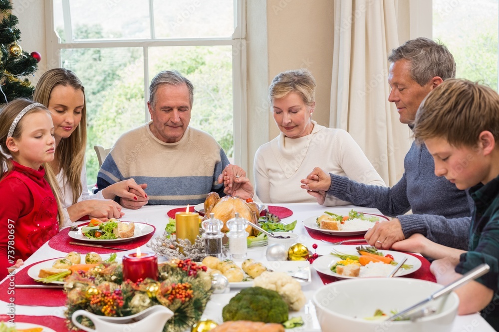 Extended family saying grace before christmas dinner