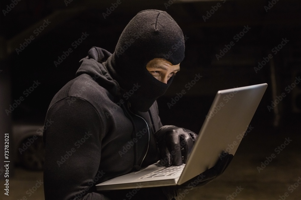 Focused burglar standing holding laptop Focused burglar standing holding laptop
