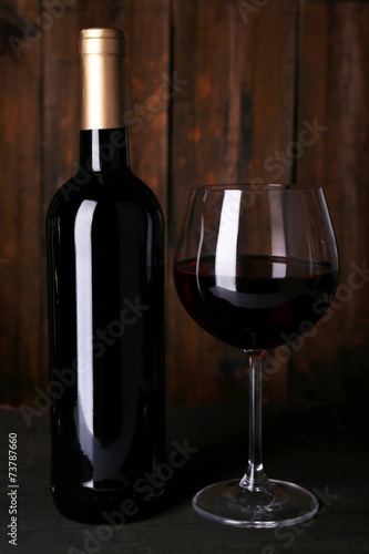 Red wine glass and bottle of wine on wooden background