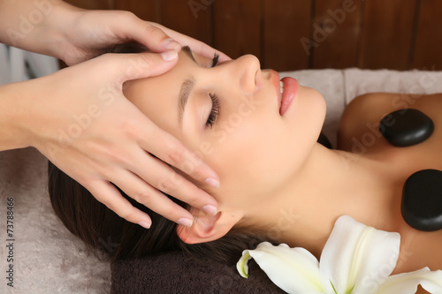 Beautiful young woman in spa salon with spa stones taking head
