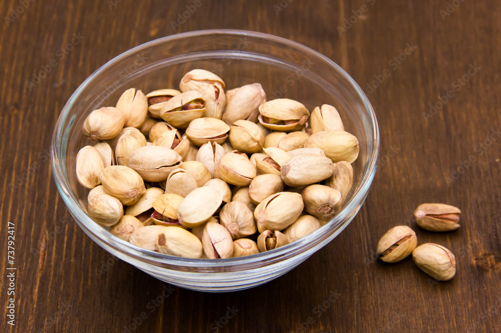 Pistachios on glass bowl on wooden table Pistachios on glass bowl on wooden table