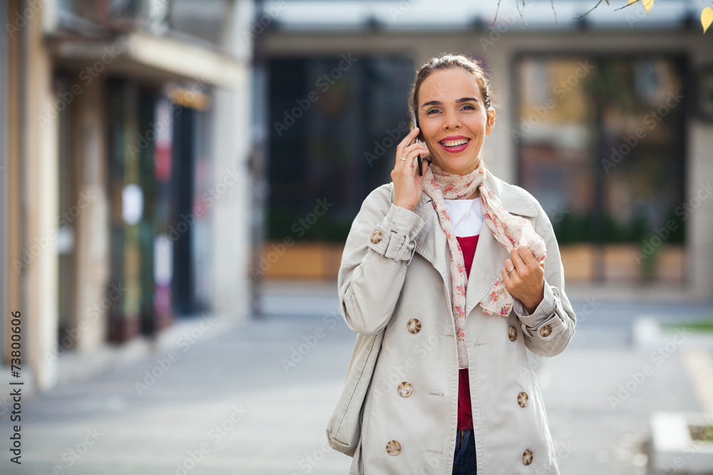 Fototapeta premium Smiling young woman on the street talking on the phone