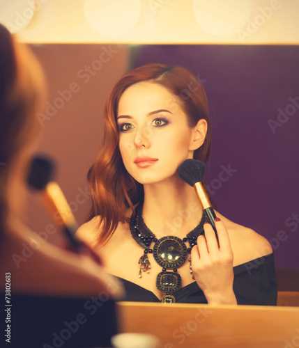 Beautiful redhead women appling makeup near mirror