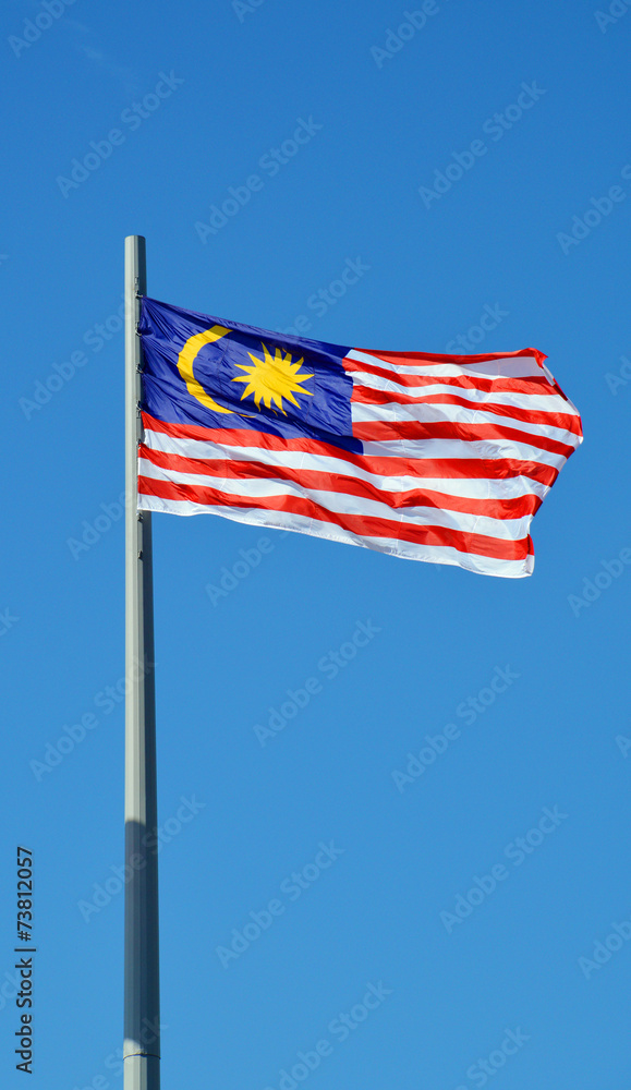 Флаг Малайзии на флагштоке на фоне голубого неба