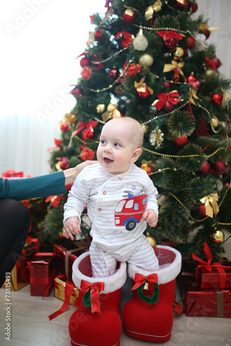 Младенец  стоит около рождественской елки