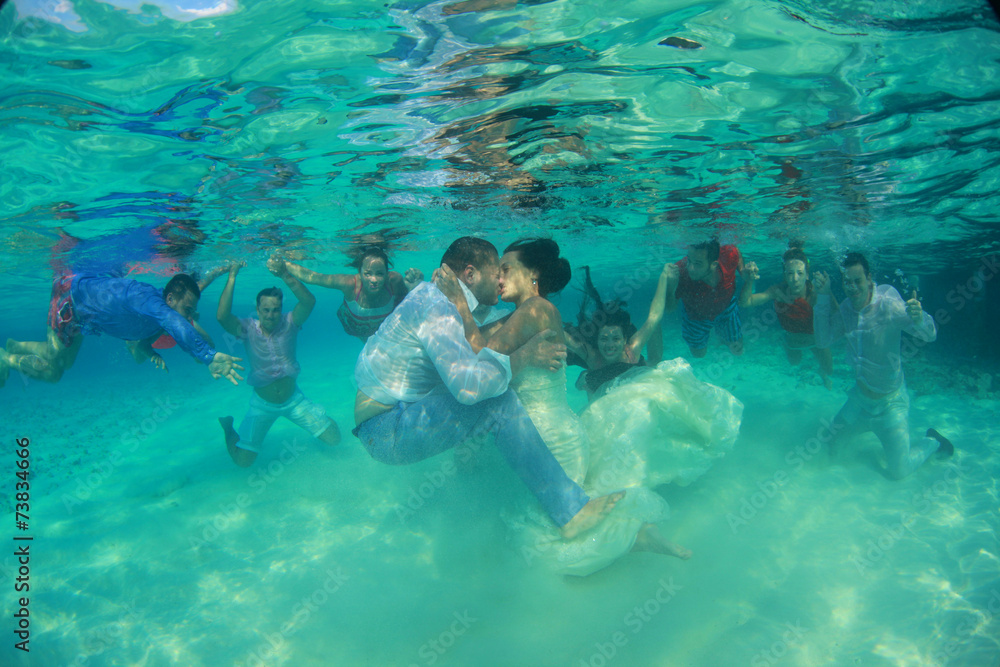 Bride and groom kissing underwater with friends witnessing