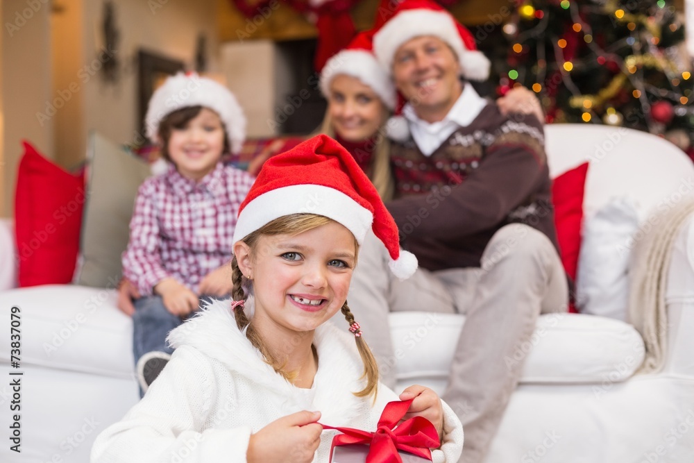Little girl opening a gift with her family behind Little girl opening a gift with her family behind
