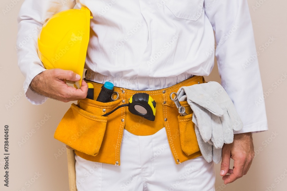 Handyman holding his yellow helmet in tool belt Handyman holding his yellow helmet in tool belt