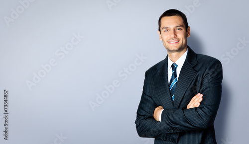 Happy businessman with crossed arms, against grey