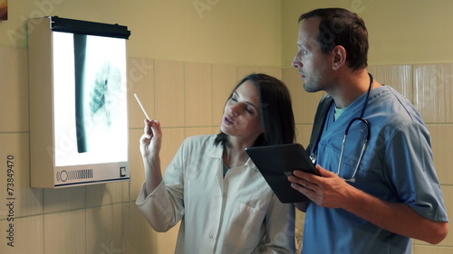 Doctors talking and checking lungs xray using tablet computer in photo