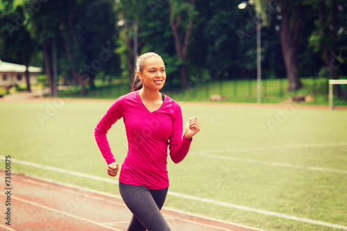 smiling woman running on track outdoors © Syda Productions