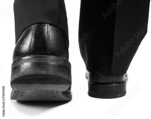 Closeup of male suit walking away in black worn shoes towards wh