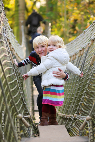 Brother and sister climbing on the rope bridge in adventure park