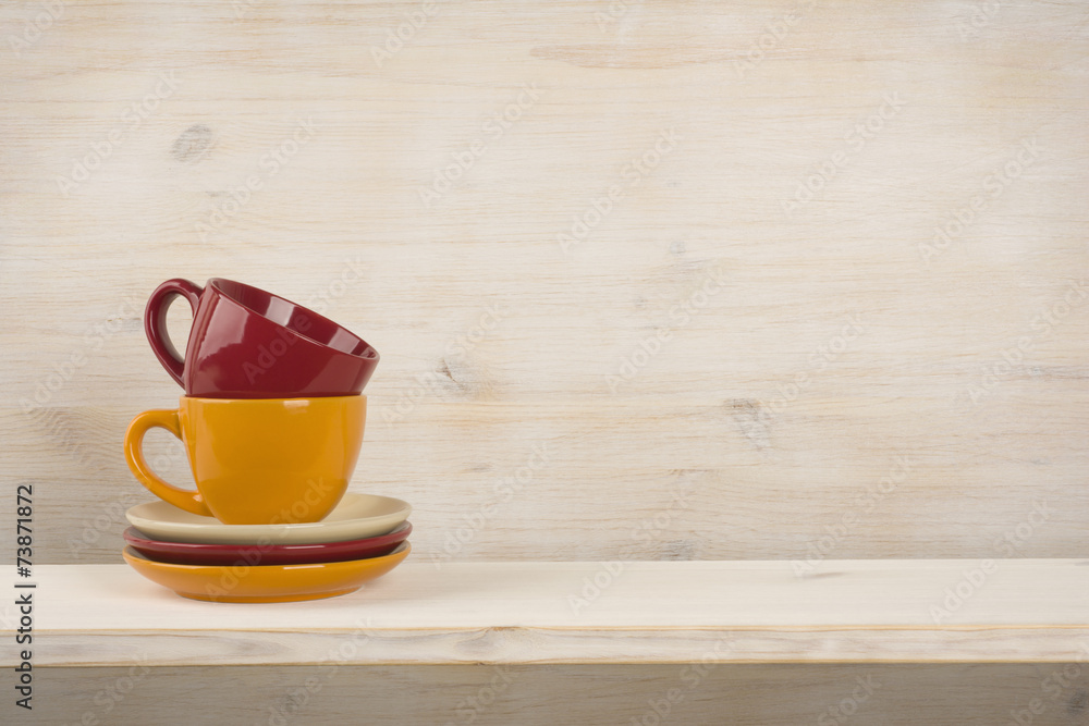Colorful coffee cups on shelf over wooden background Colorful coffee cups on shelf over wooden background