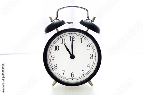 Oldfashioned black glossy alarm clock showing 11 o'clock