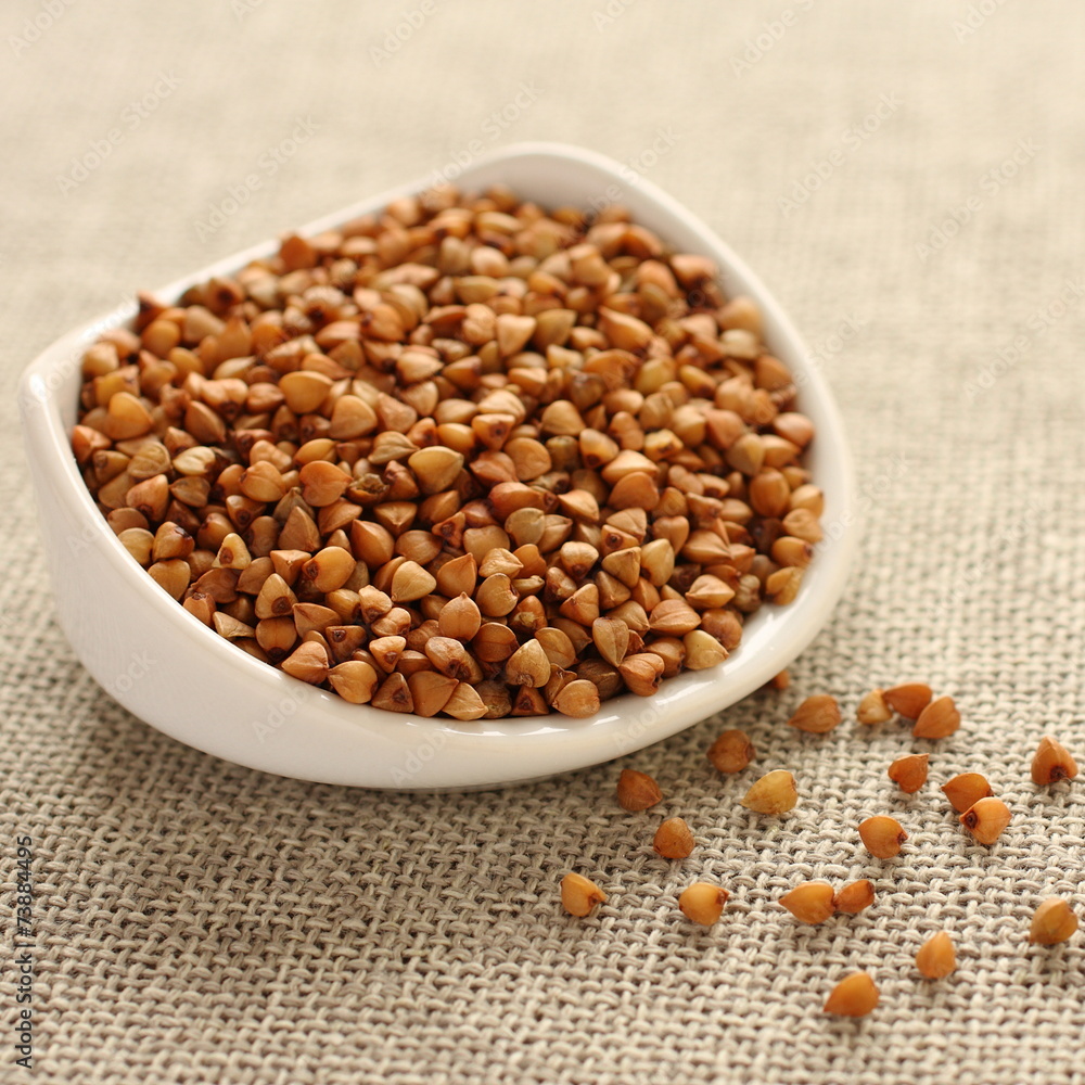 Buckwheat grains in white ceramic bowl on sackcloth background Buckwheat grains in white ceramic bowl on sackcloth background