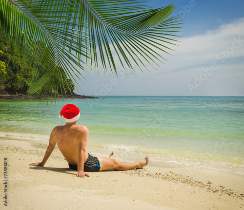 Man on the tropical beach in Santa Claus hat
