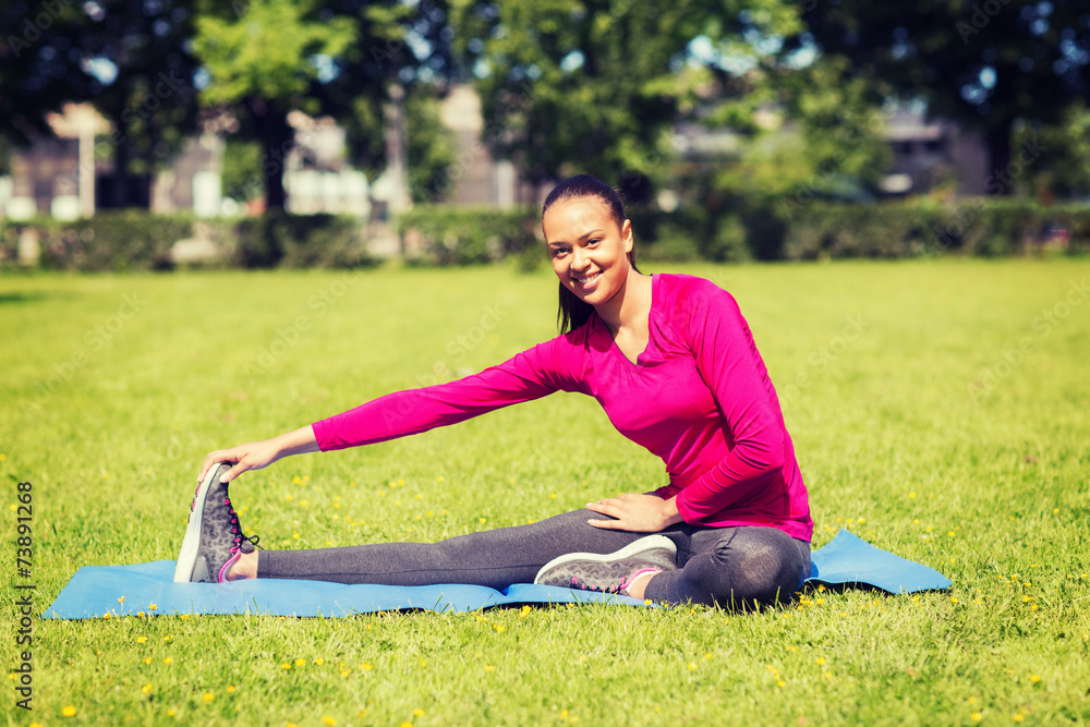 smiling woman stretching leg on mat outdoors