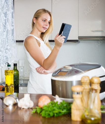  housewife reading ereader and cooking with multicooker photo