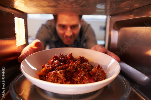 Man Putting Leftover Chili Into Microwave Oven To Cook photo