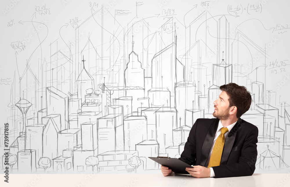 Businessman sitting at the white table with hand drawn buildings Businessman sitting at the white table with hand drawn buildings