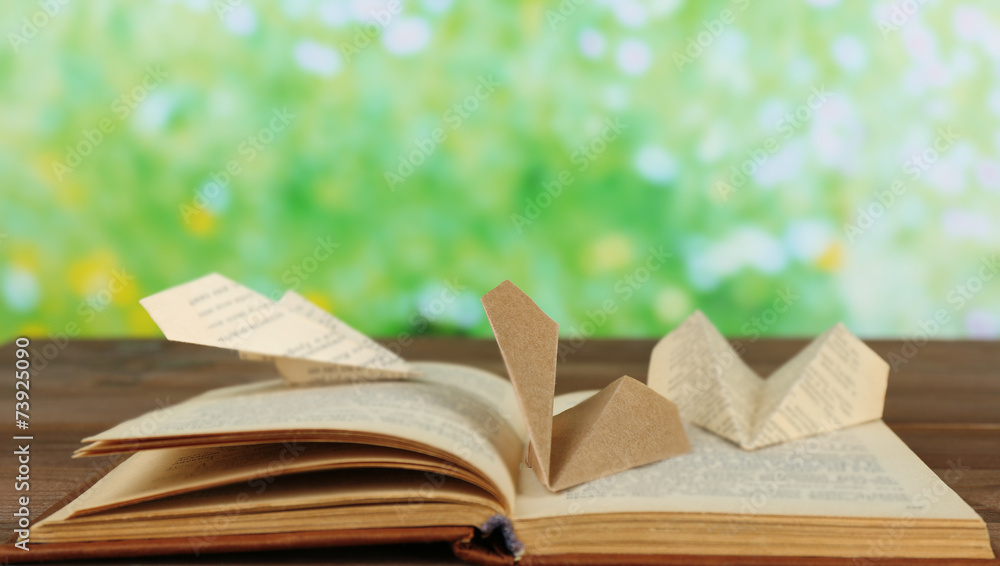 Origami airplanes on old book, on wooden table, outdoors Origami airplanes on old book, on wooden table, outdoors