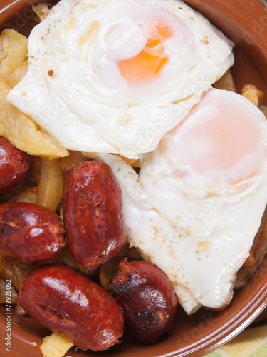 Eggs with french fries and small sausages.