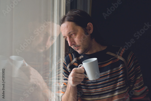 Fotografi Sad man by the window drinking coffee