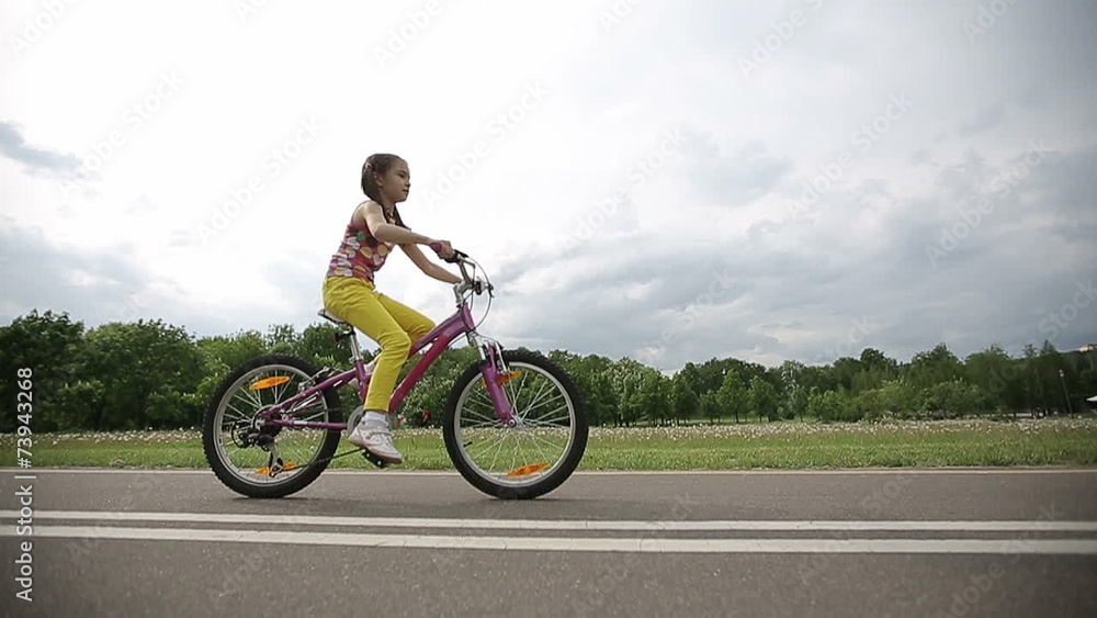 Little girl cycling in park on a pink bike in slow motion Little girl cycling in park on a pink bike in slow motion