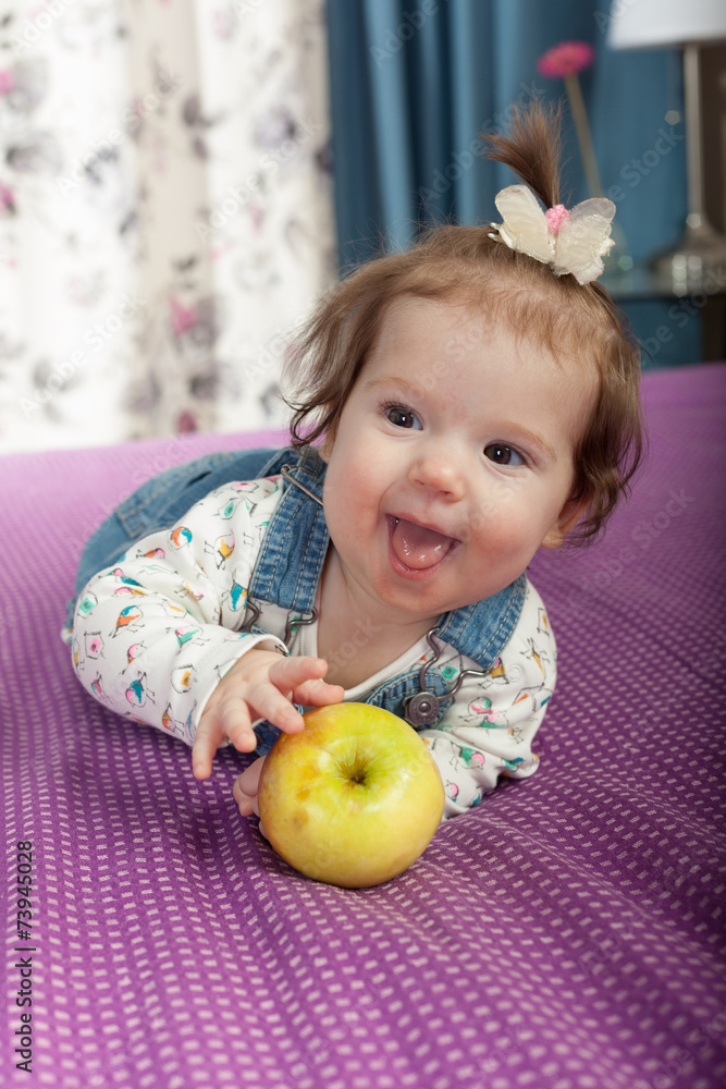 Fototapeta premium Little baby girl with an apple smiling indoors