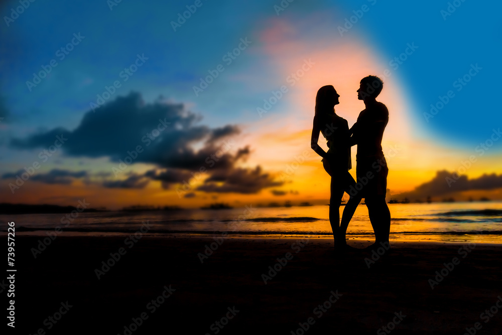 silhouettes of young loving couple on bright sunset sky and sea