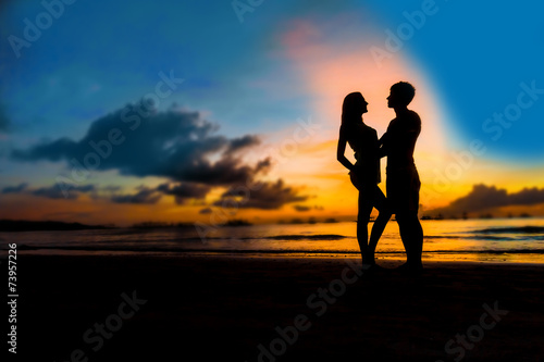silhouettes of young loving couple on bright sunset sky and sea