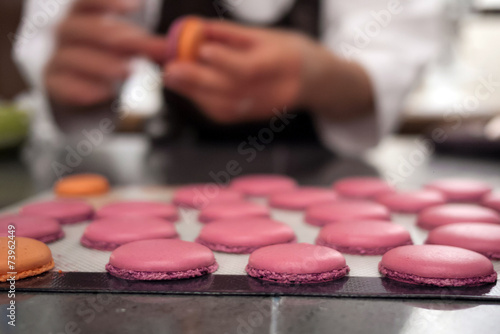 Baker placing macaron cookies on sheet for baking, with baker bl