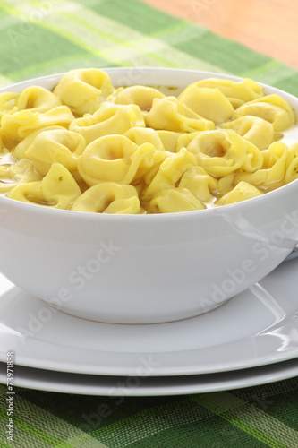 Bowl of chicken broth and tortellini on a green tablecloth.
