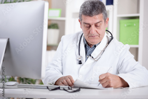 physician with stethoscope around his neck working in office