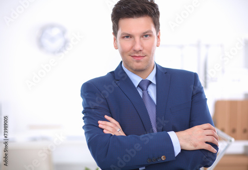 Business man or manager standing against his desk at office with