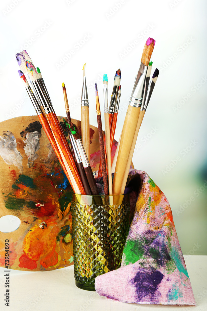 Paint brushes with paints and palette on bright background Paint brushes with paints and palette on bright background