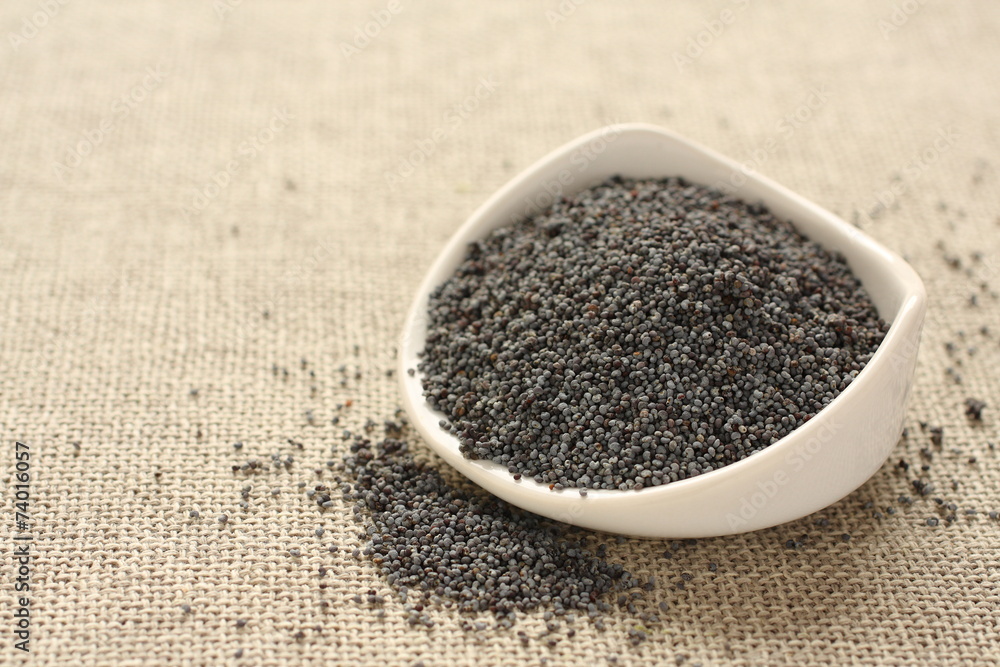 Poppy seeds in white ceramic bowl on sackcloth background Poppy seeds in white ceramic bowl on sackcloth background