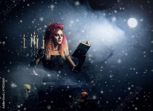 Beautiful witch making witchcraft on a snowy background