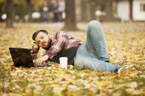 Man Laying Down In Autumn Leaves Using Laptop Computer