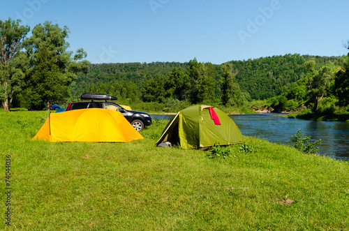 Tourist camp with tents and car on the river bank