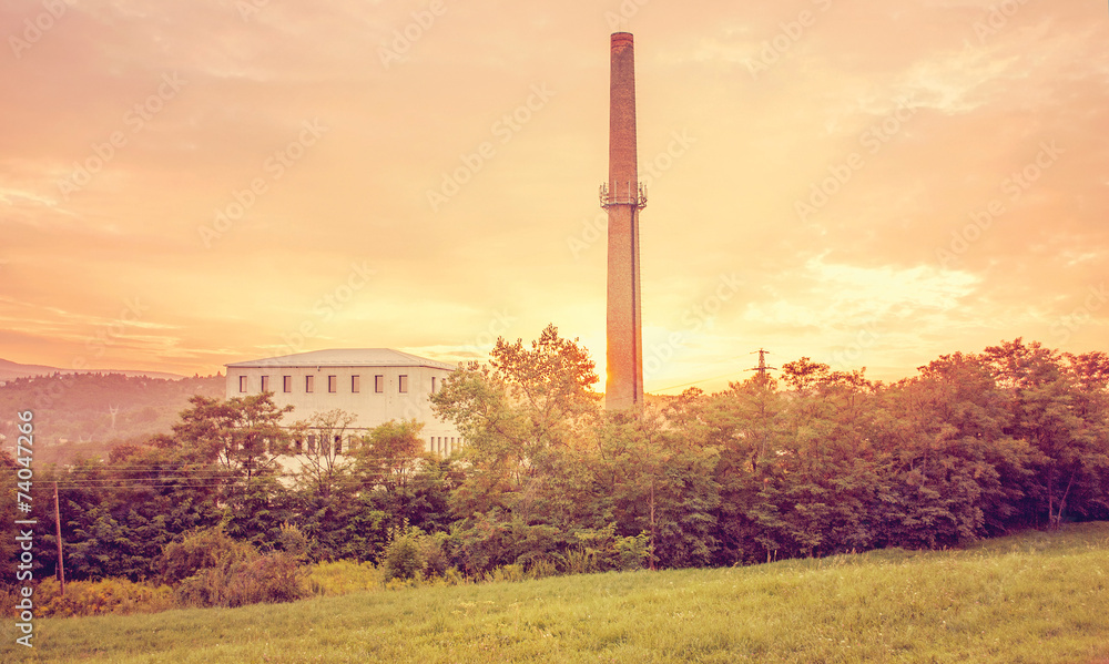 Factory building at summer sunset behind trees