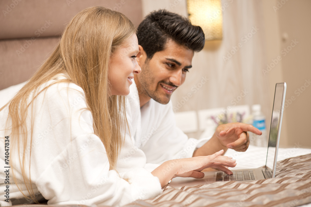 happy young couple browsing online in bed / online shopping happy young couple browsing online in bed / online shopping