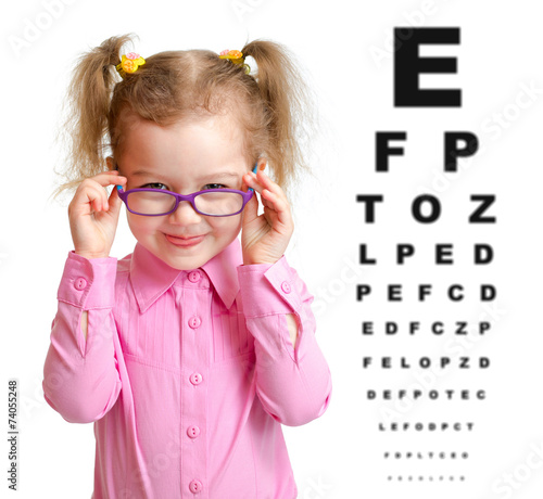 Smiling girl putting on glasses with blurry eye chart behind her