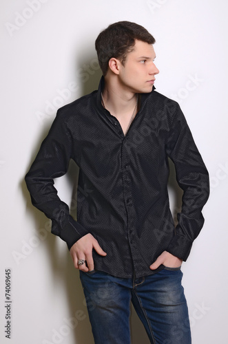 Fashion portrait of young man in black shirt poses over wall