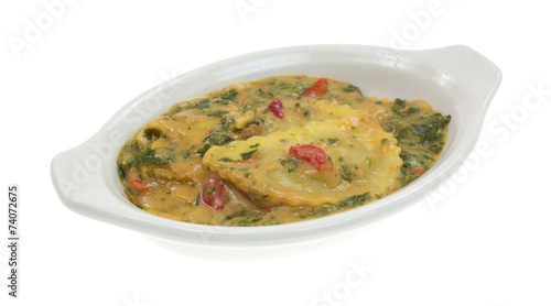 A baking dish with cooked ravioli in wine sauce with spinach
