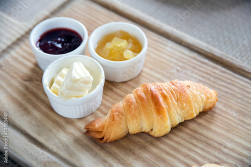croissants with butter, strawberry jam and pineapple jam in white cup on wooden tray for morning breakfast