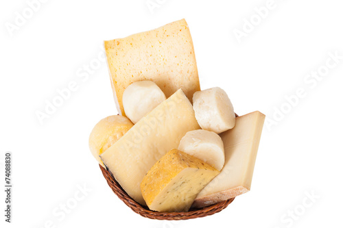 Different cheeses and a bunch of parsley lying in a wicker baske